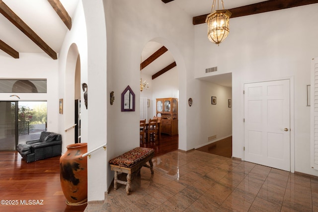 foyer with high vaulted ceiling, arched walkways, an inviting chandelier, beamed ceiling, and visible vents