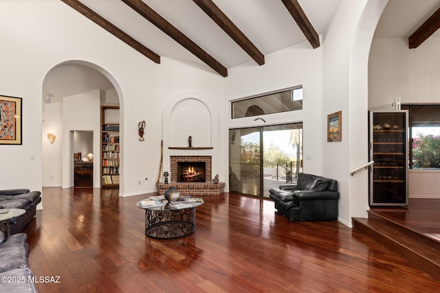 living room featuring high vaulted ceiling, wood finished floors, arched walkways, a brick fireplace, and beam ceiling