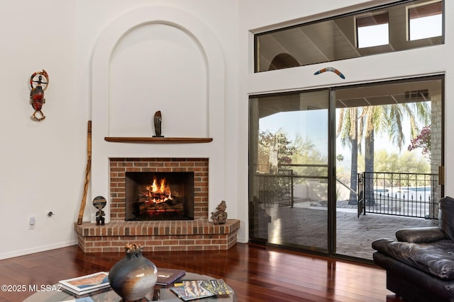 living area featuring wood-type flooring, a brick fireplace, and baseboards