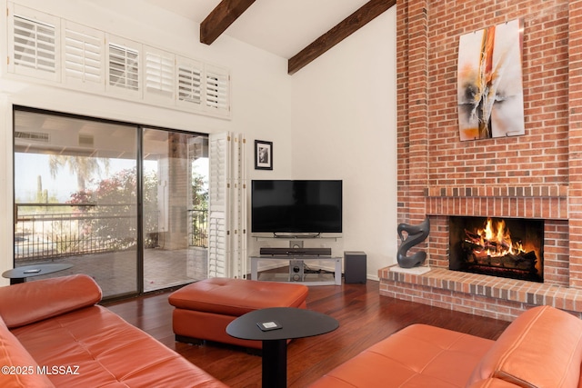 living area with a towering ceiling, a brick fireplace, wood finished floors, and beam ceiling