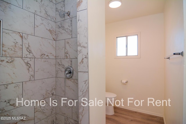 bathroom with toilet, tiled shower, wood finished floors, and baseboards