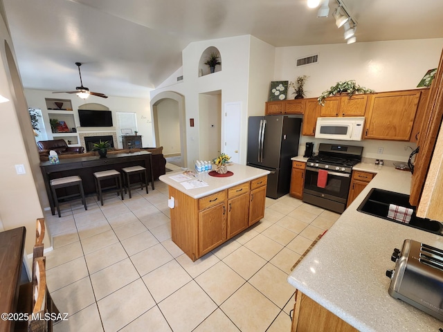60464 E Blackcrest Loop, Tucson, AZ 85739 - kitchen featuring visible vents, arched walkways, stainless steel gas stove, white microwave, and freestanding refrigerator