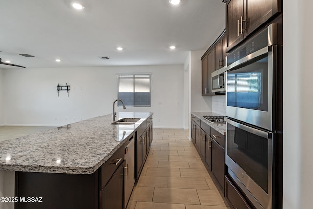 3352 W Shadow Park Way, Tucson, AZ 85742 - kitchen with appliances with stainless steel finishes, a sink, dark brown cabinets, light stone countertops, and a center island with sink