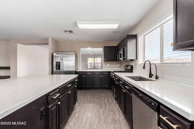 kitchen with a sink, dark cabinetry, light wood finished floors, stainless steel appliances, and visible vents