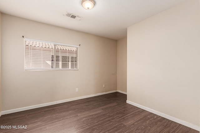 spare room with dark wood finished floors, visible vents, and baseboards