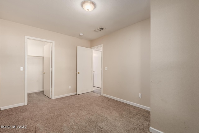 unfurnished bedroom featuring visible vents, a walk in closet, a closet, baseboards, and carpet flooring