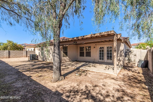 rear view of property with stucco siding, a fenced backyard, and french doors