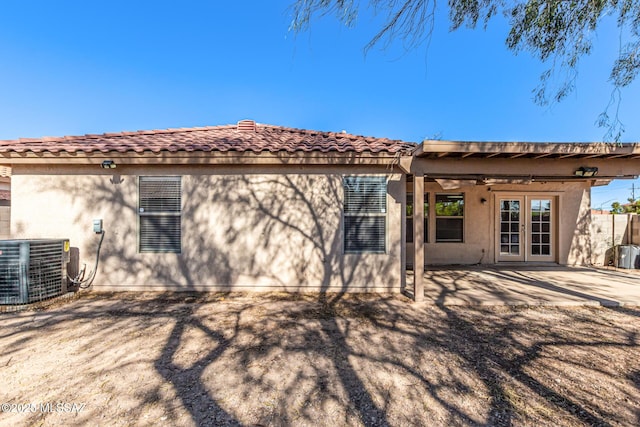 back of house with central AC unit, stucco siding, a tile roof, french doors, and a patio