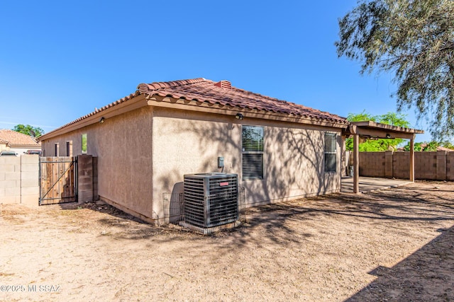 rear view of property featuring a gate, stucco siding, central AC unit, and fence