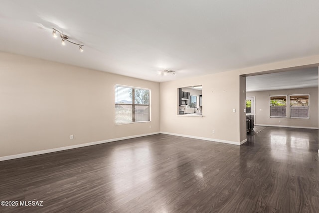 spare room featuring rail lighting, baseboards, and dark wood-style flooring