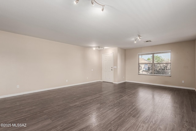 unfurnished room featuring dark wood-type flooring, track lighting, visible vents, and baseboards