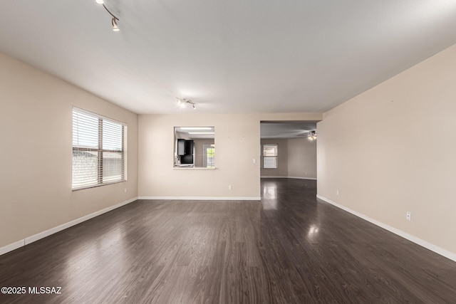unfurnished living room with track lighting, baseboards, dark wood-style floors, and plenty of natural light