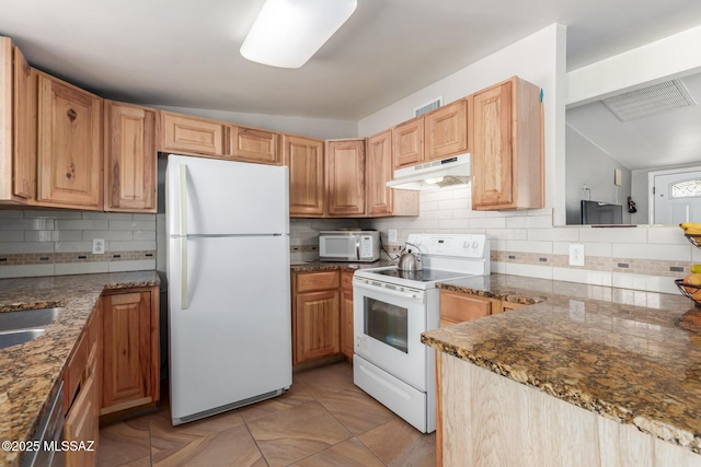 kitchen featuring backsplash, dark stone countertops, under cabinet range hood, and white appliances