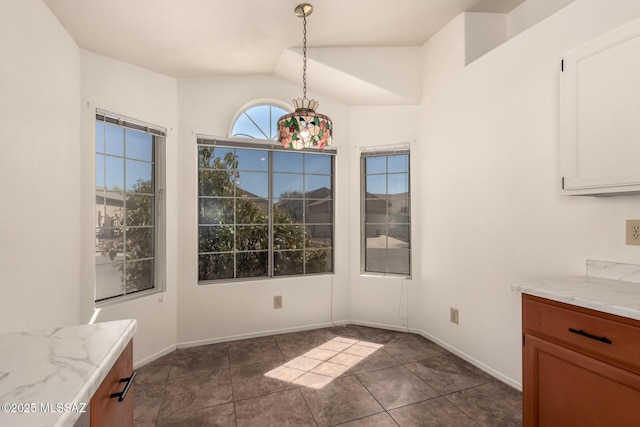 unfurnished dining area featuring vaulted ceiling, baseboards, and dark tile patterned flooring