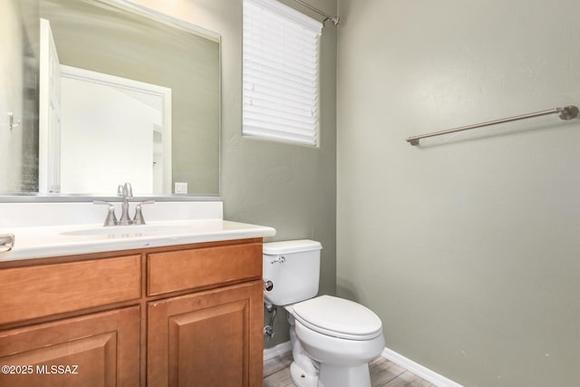 half bath featuring baseboards, wood finished floors, toilet, and vanity