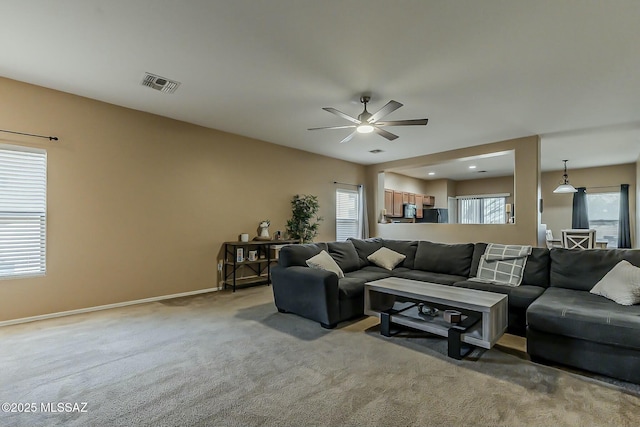 living area with baseboards, visible vents, a ceiling fan, and light colored carpet