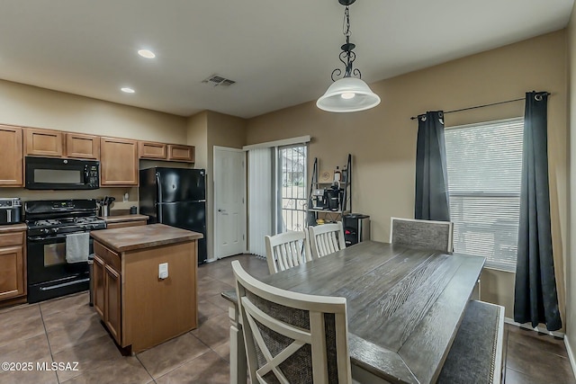kitchen with black appliances, decorative light fixtures, tile patterned flooring, visible vents, and a kitchen island