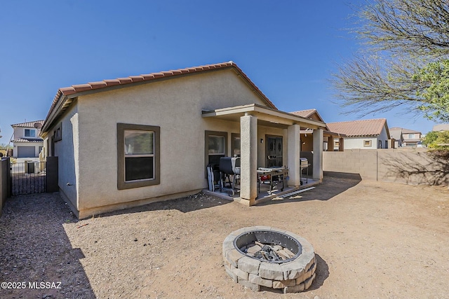 back of house featuring a fire pit, a tiled roof, a fenced backyard, and stucco siding
