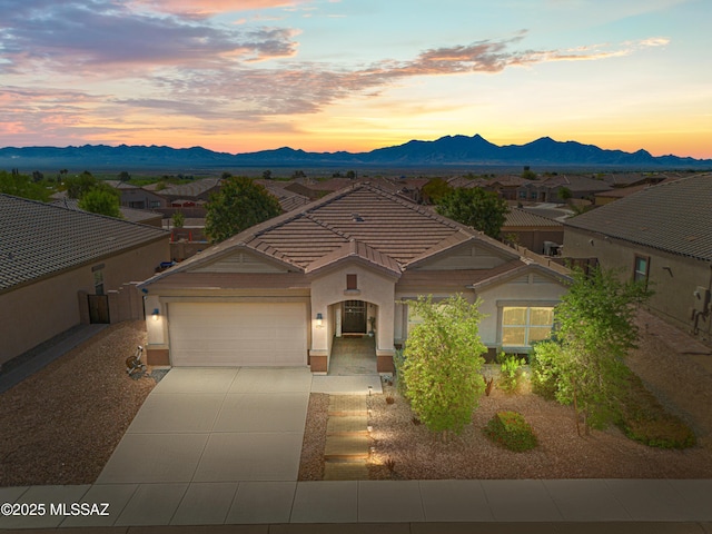 view of front of house with driveway, a tiled roof, a mountain view, a garage, and stucco siding