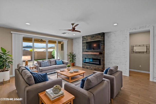 living room with a ceiling fan, light wood-style flooring, a fireplace, baseboards, and visible vents