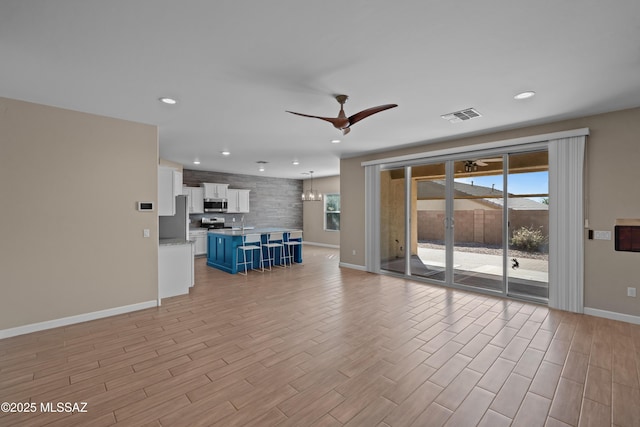 unfurnished living room with light wood finished floors, baseboards, visible vents, and ceiling fan