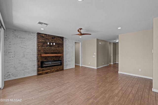 unfurnished living room featuring wood finished floors, ceiling fan, a large fireplace, baseboards, and visible vents