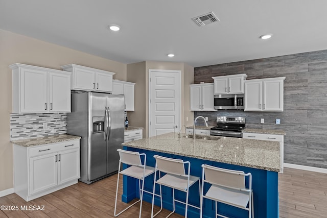 kitchen featuring a sink, visible vents, light wood-style floors, decorative backsplash, and appliances with stainless steel finishes