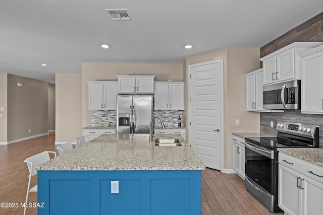 kitchen featuring a sink, baseboards, light wood-style flooring, tasteful backsplash, and appliances with stainless steel finishes