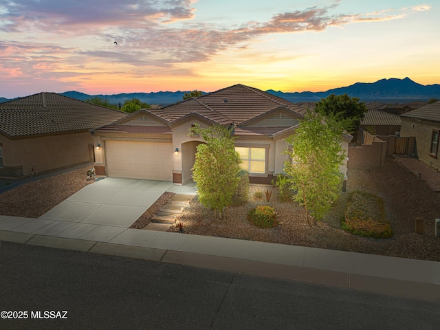 view of front of property with a tiled roof, stucco siding, an attached garage, concrete driveway, and a mountain view