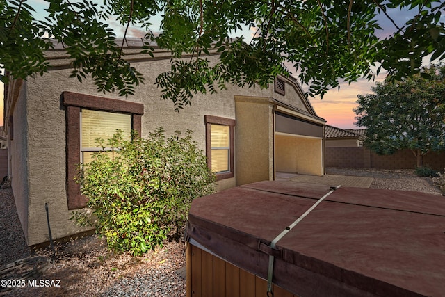 view of home's exterior with fence, a patio area, a hot tub, and stucco siding