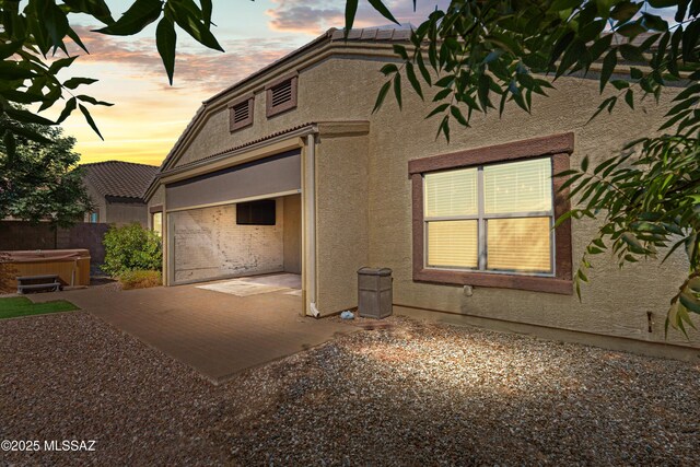 property exterior at dusk featuring stucco siding, a hot tub, and a patio area
