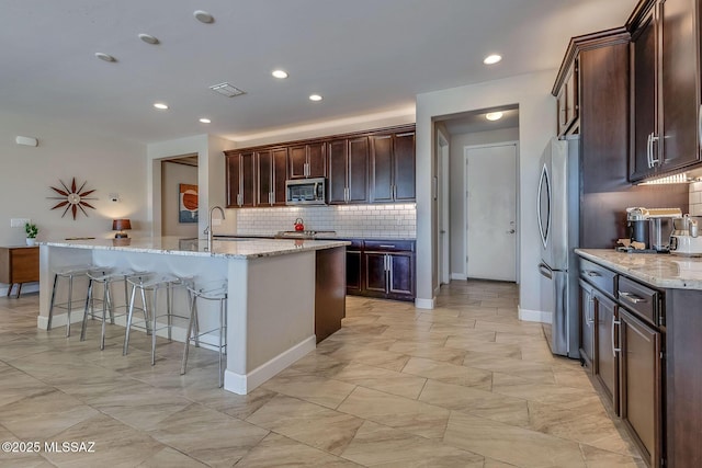 kitchen with a breakfast bar area, an island with sink, stainless steel appliances, tasteful backsplash, and visible vents