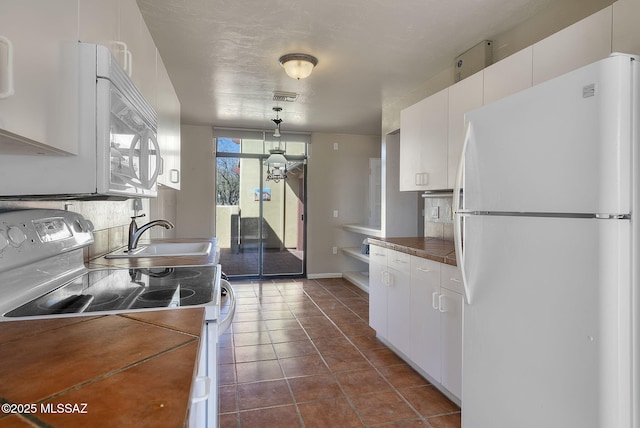 kitchen featuring dark countertops, a sink, white appliances, white cabinets, and visible vents
