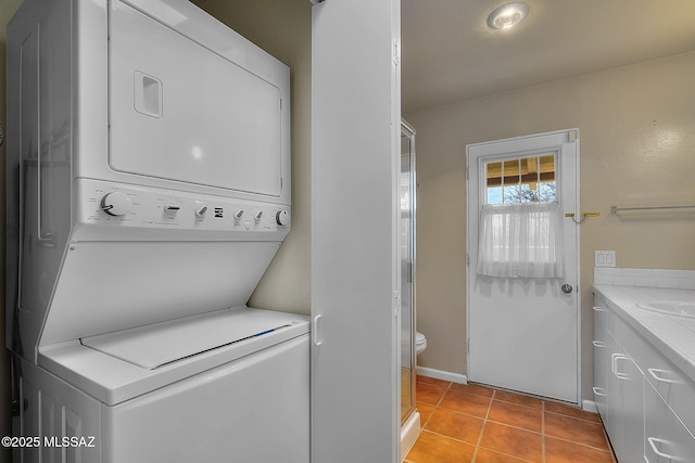 washroom featuring baseboards, light tile patterned flooring, stacked washing maching and dryer, and laundry area
