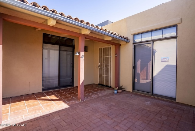 view of exterior entry with stucco siding and a patio