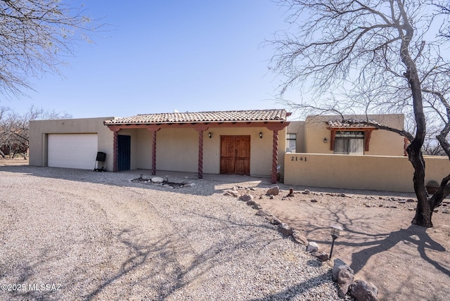 pueblo-style house featuring a garage, driveway, stucco siding, and fence