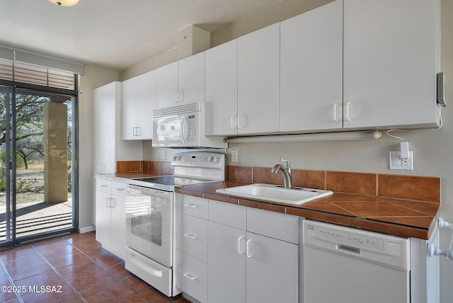 kitchen with dark tile patterned flooring, white appliances, a sink, and white cabinetry