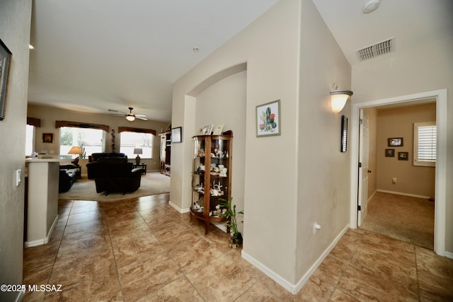 hallway with visible vents, baseboards, and light carpet