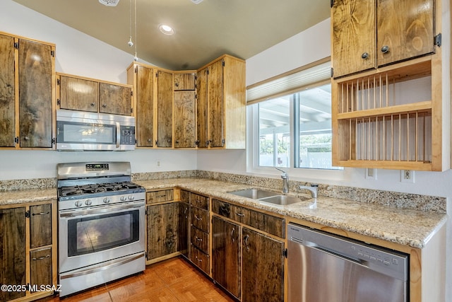 kitchen with a sink, lofted ceiling, light stone counters, open shelves, and appliances with stainless steel finishes