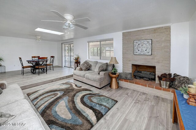 living room with wood finished floors, ceiling fan, a skylight, and a brick fireplace