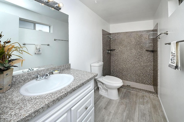 bathroom featuring toilet, a tile shower, wood finished floors, and vanity