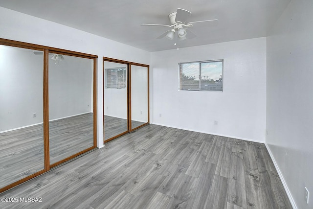 unfurnished bedroom with wood finished floors, multiple closets, a ceiling fan, and baseboards