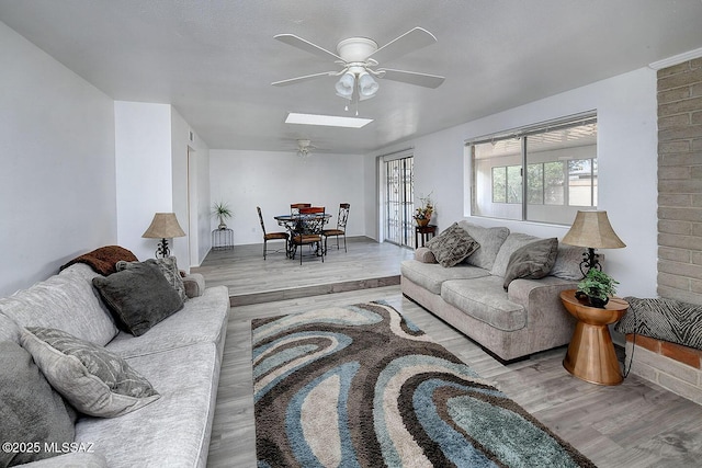 living area featuring wood finished floors, a ceiling fan, and a skylight