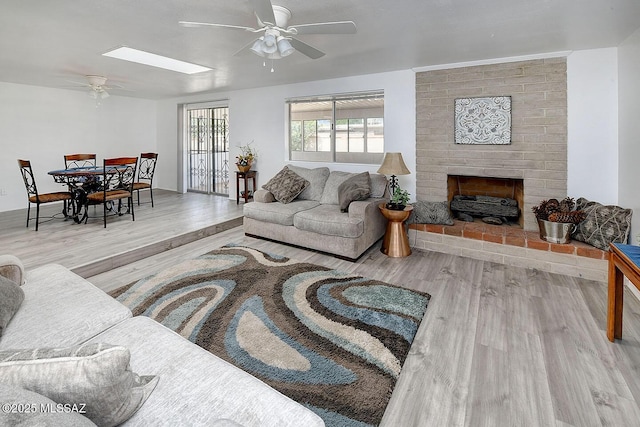 living room with a fireplace, wood finished floors, a ceiling fan, and a skylight