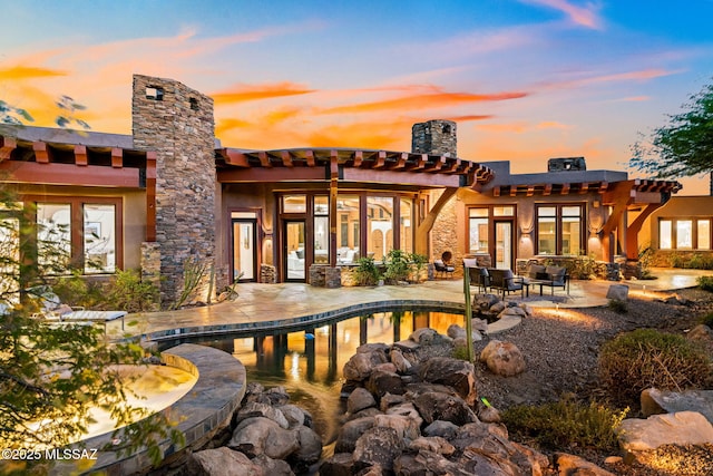 back of property at dusk featuring an outdoor pool, a chimney, and a patio