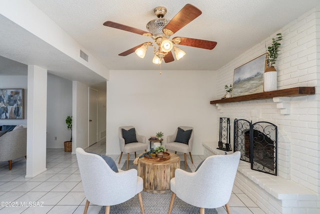 living area featuring a fireplace, light tile patterned floors, ceiling fan, and visible vents