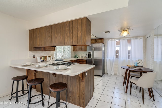 kitchen featuring a kitchen breakfast bar, appliances with stainless steel finishes, visible vents, light countertops, and a peninsula