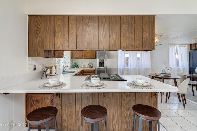kitchen featuring brown cabinetry, appliances with stainless steel finishes, light countertops, a sink, and a peninsula