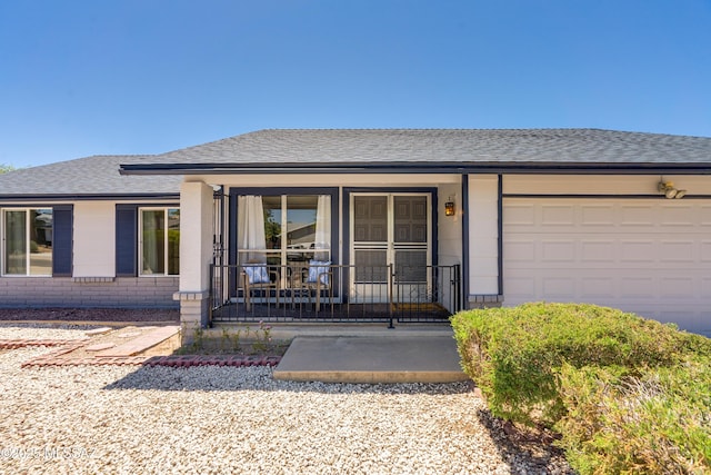 property entrance featuring an attached garage, a porch, a shingled roof, and brick siding