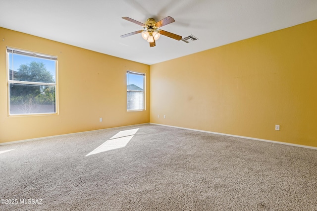 carpeted spare room with ceiling fan, baseboards, visible vents, and plenty of natural light